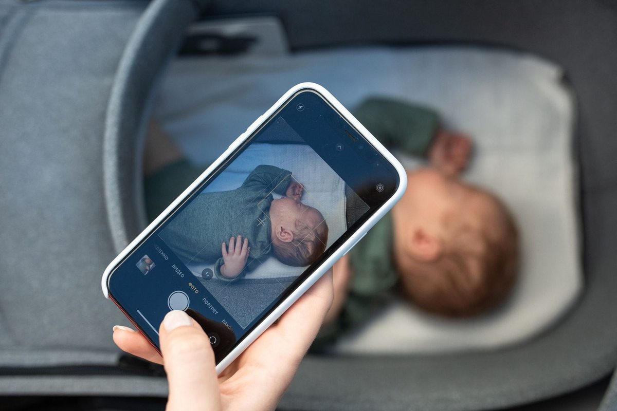 Main tenant smartphone montrant photo d'enfant endormi dans lit d'enfant