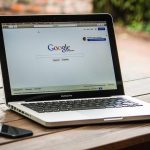 Laptop ouvert sur Google, smartphone à gauche, sur une table en bois