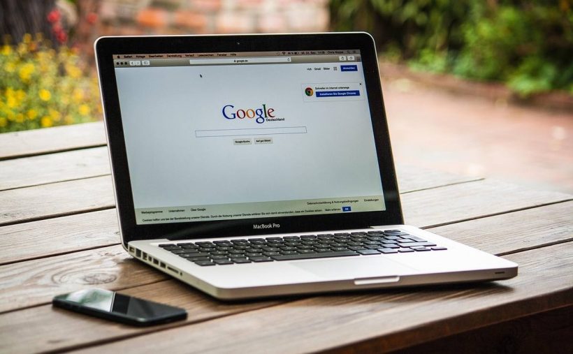 Laptop ouvert sur Google, smartphone à gauche, sur une table en bois