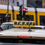 Un taxi jaune avec panneau sur le toit, rue avec tram et feu rouge