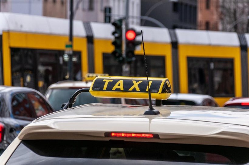 Un taxi jaune avec panneau sur le toit, rue avec tram et feu rouge