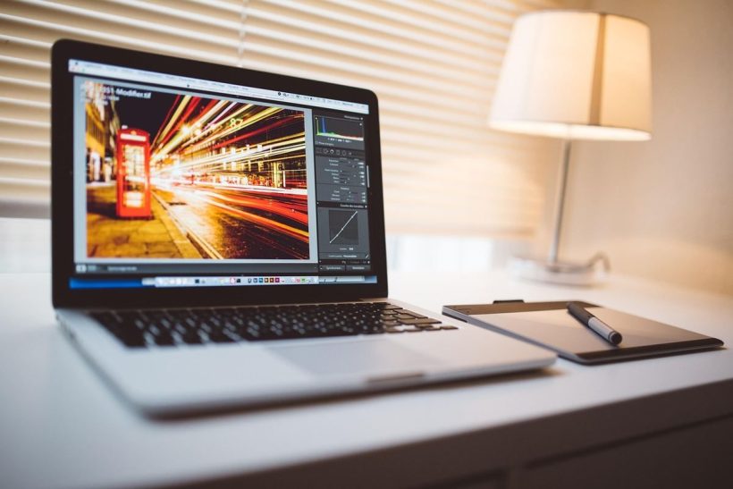 Un ordinateur portable sur un bureau, une lampe allumée, une photo en cours d'édition