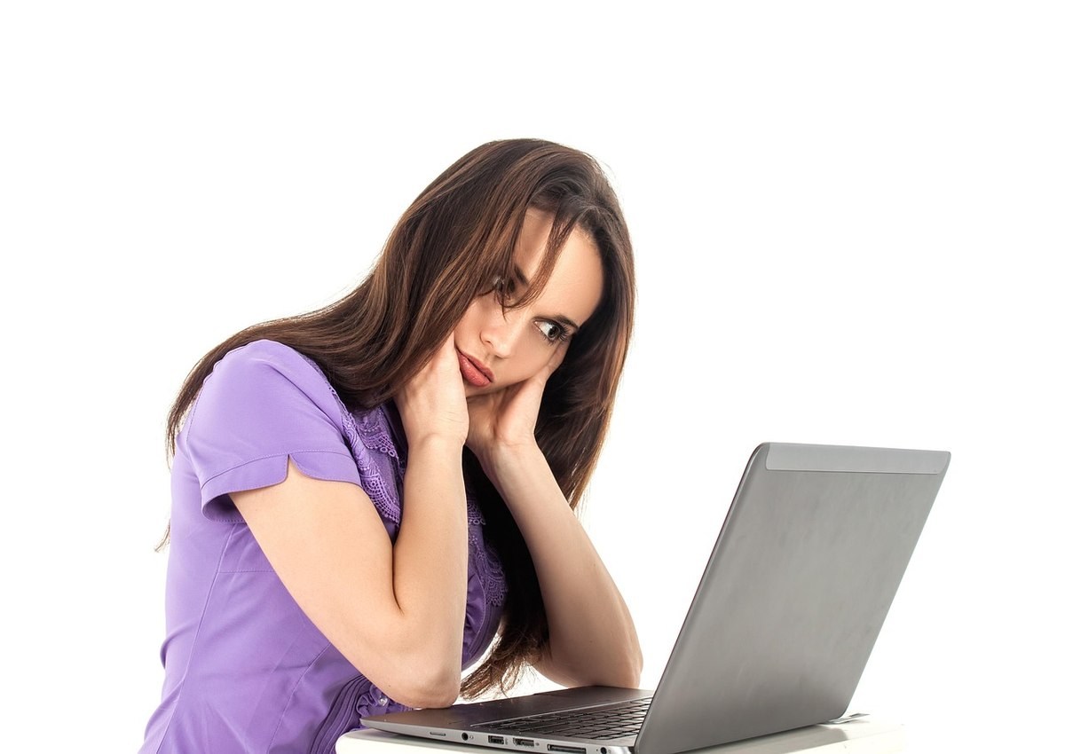 Une femme en violet repose la tête sur la main devant un ordinateur Une femme en violet repose la tête sur la main devant un ordinateur