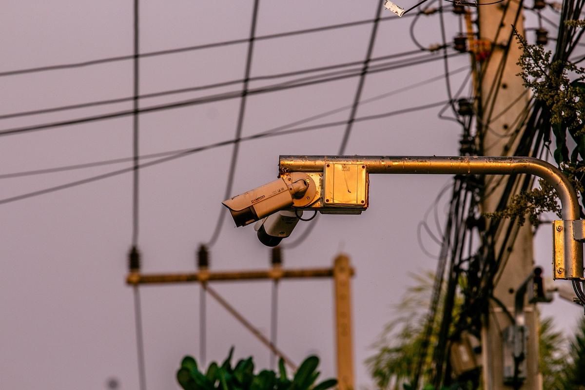 Caméra de surveillance fixée à un bras doré sur un poteau, fils électriques en arrière-plan Caméra de surveillance fixée à un bras doré sur un poteau, fils électriques en arrière-plan